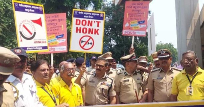 Image of Nagpur police officers holding a sign promoting the No Honking Campaign, with a busy urban background.