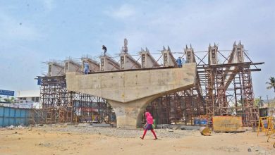 A depiction of a flyover under construction, with workers installing monopoles to raise high-tension wires.