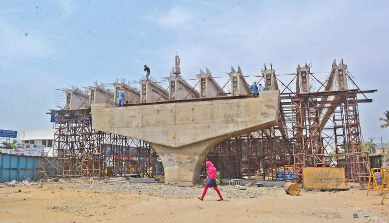 A depiction of a flyover under construction, with workers installing monopoles to raise high-tension wires.