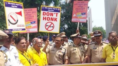 Image of Nagpur police officers holding a sign promoting the No Honking Campaign, with a busy urban background.